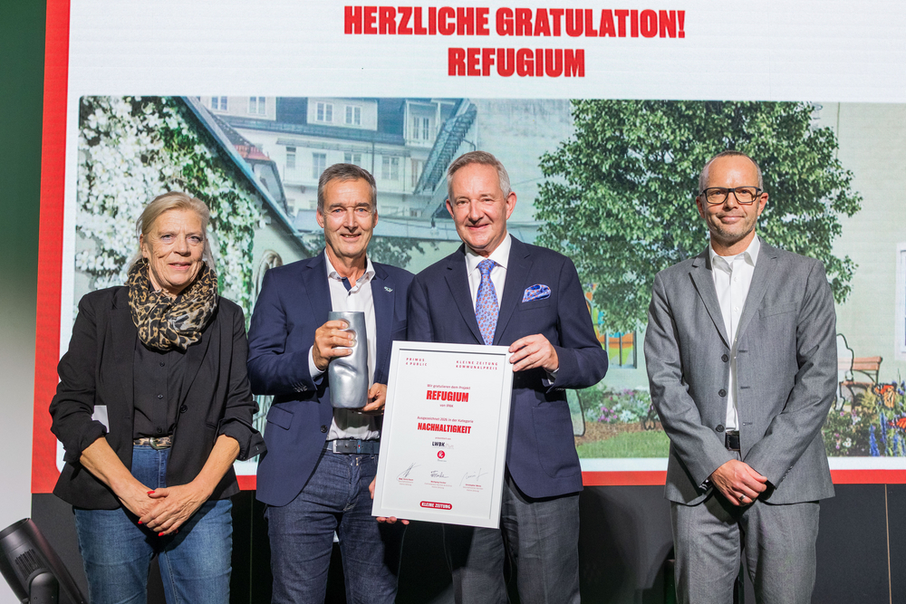 Refugium-Preis: Preisträger mit Urkunde und Pokal vor Hintergrundwand