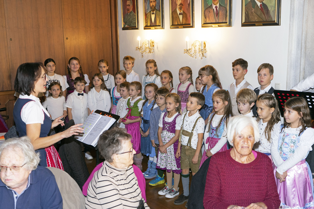 Kinderchor mit Dirigentin und älteren Damen in traditioneller Kleidung, Österreich